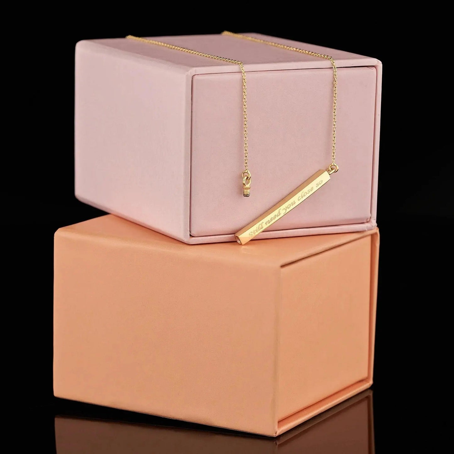 Gold bar necklace on pink and peach boxes showcasing personalization cremation urn features