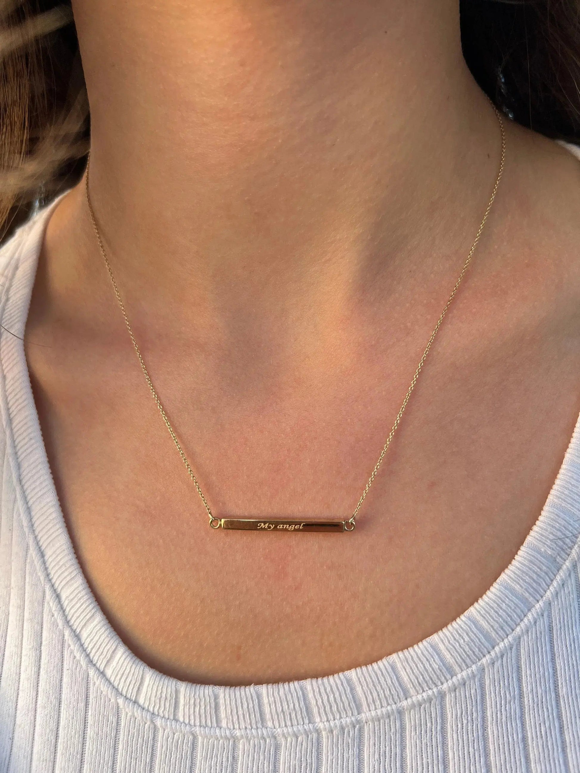 Delicate gold bar necklace featuring text engraving worn over a white ribbed top
